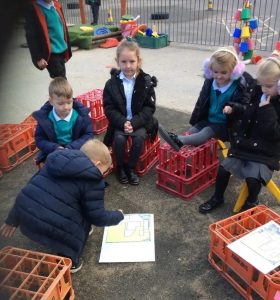 Children from Gomersal St. Mary's sitting on crates in the playground looking at a map of their school